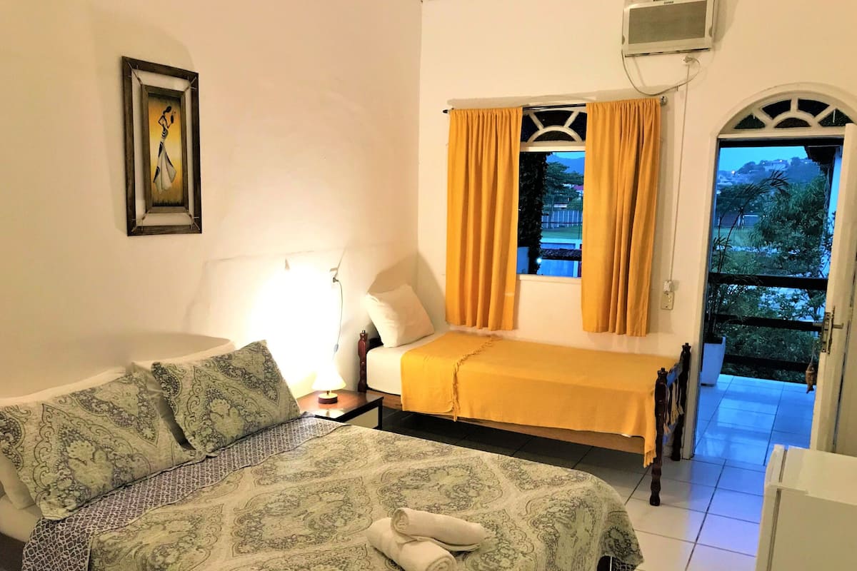 Une chambre d’hôtel avec un lit, une table de chevet avec une lampe, une fenêtre avec des rideaux et une vue sur l’extérieur.