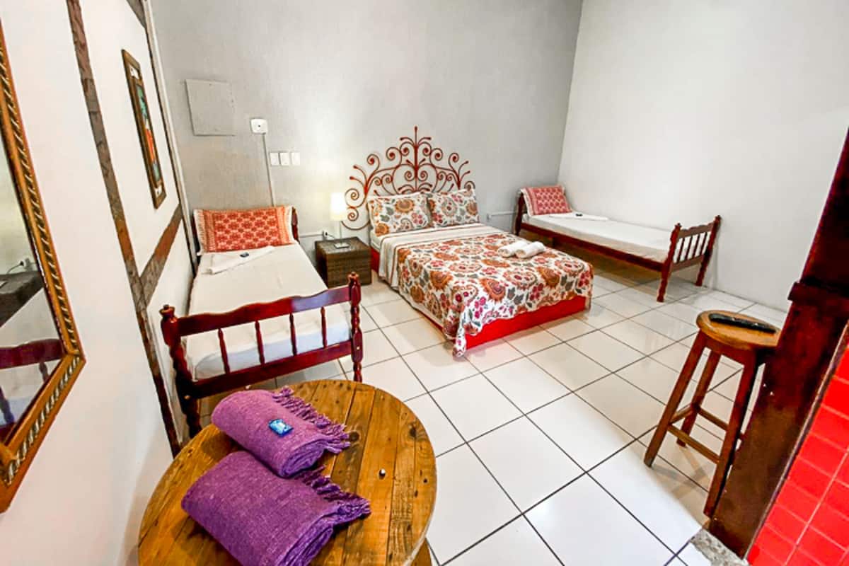 Une chambre avec deux lits, une chaise en bois, une petite table sur laquelle est posée une serviette violette, et un miroir.