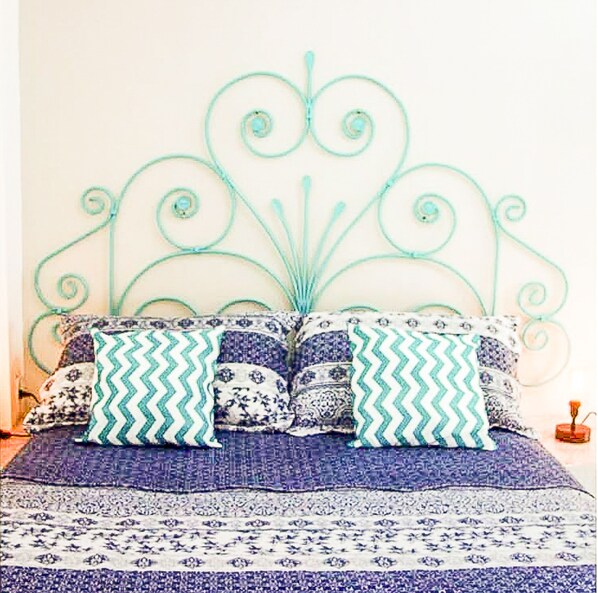 Un lit avec une tête de lit en métal, une literie à motifs et des coussins décoratifs.