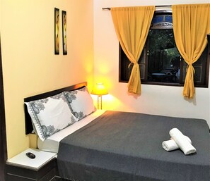 Un lit bien fait, recouvert d’une couvre-lit à motifs, une lampe de chevet et une télécommande posées sur la table de chevet.