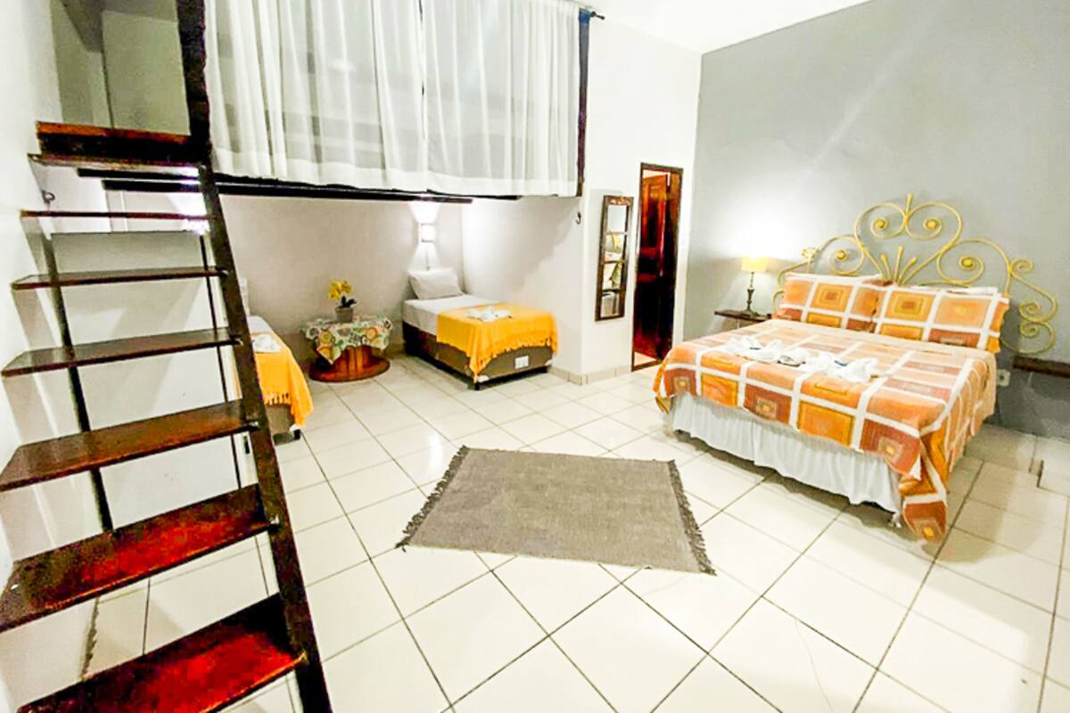 Une chambre à coucher avec un lit, une petite table avec une lampe, une chaise, une échelle et une fenêtre avec des rideaux.