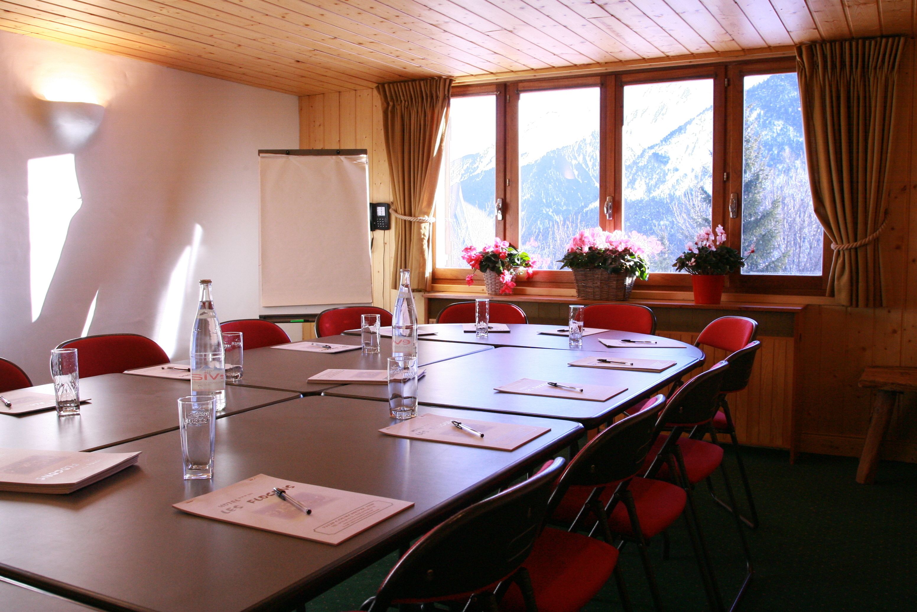 A conference room with a long table, red chairs, and a view of mountains through large windows.