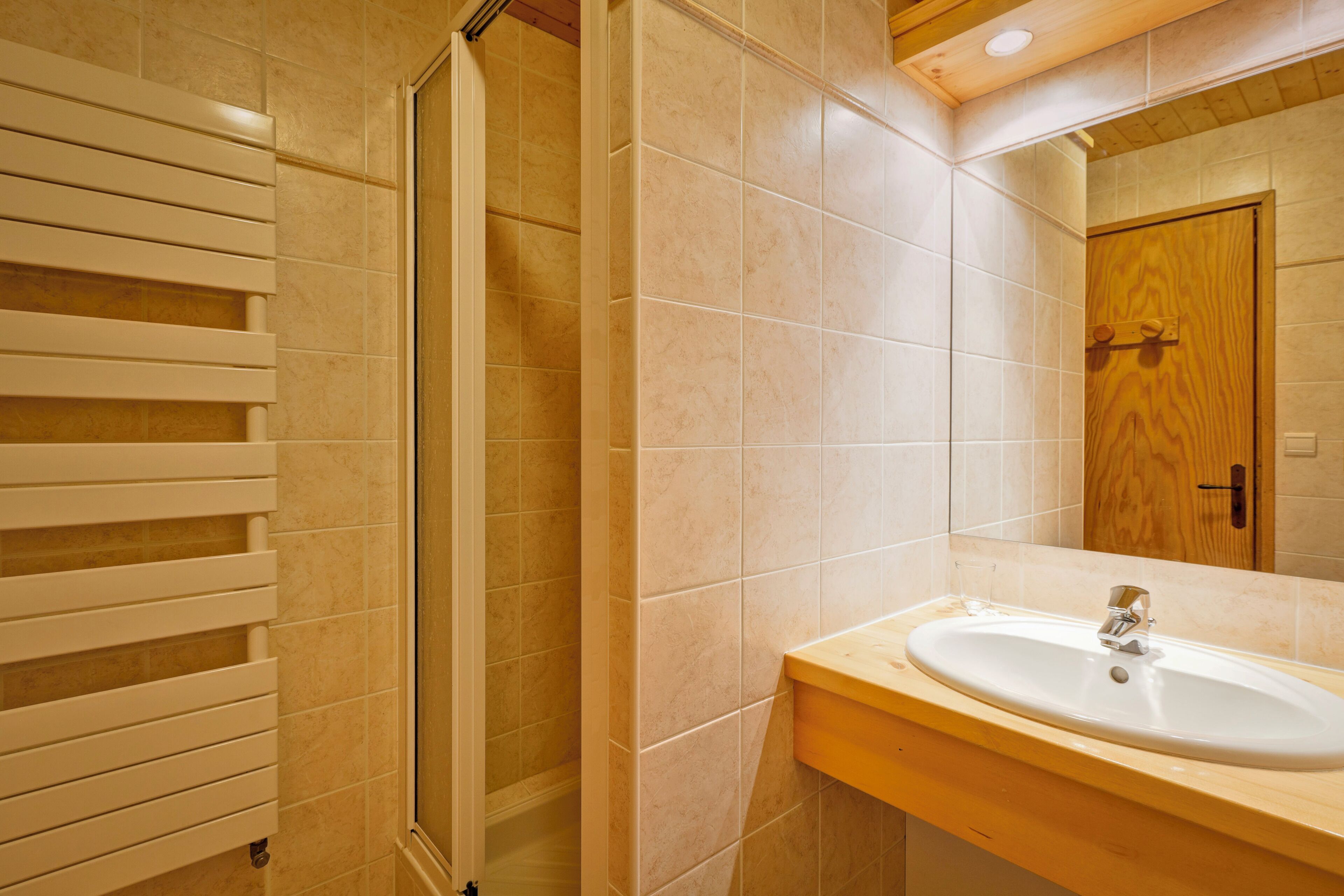 A bathroom with a shower, a sink, and a wooden door.