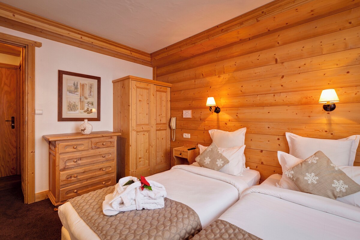 A wooden-paneled room with two beds, a wooden dresser, and a framed picture on the wall.