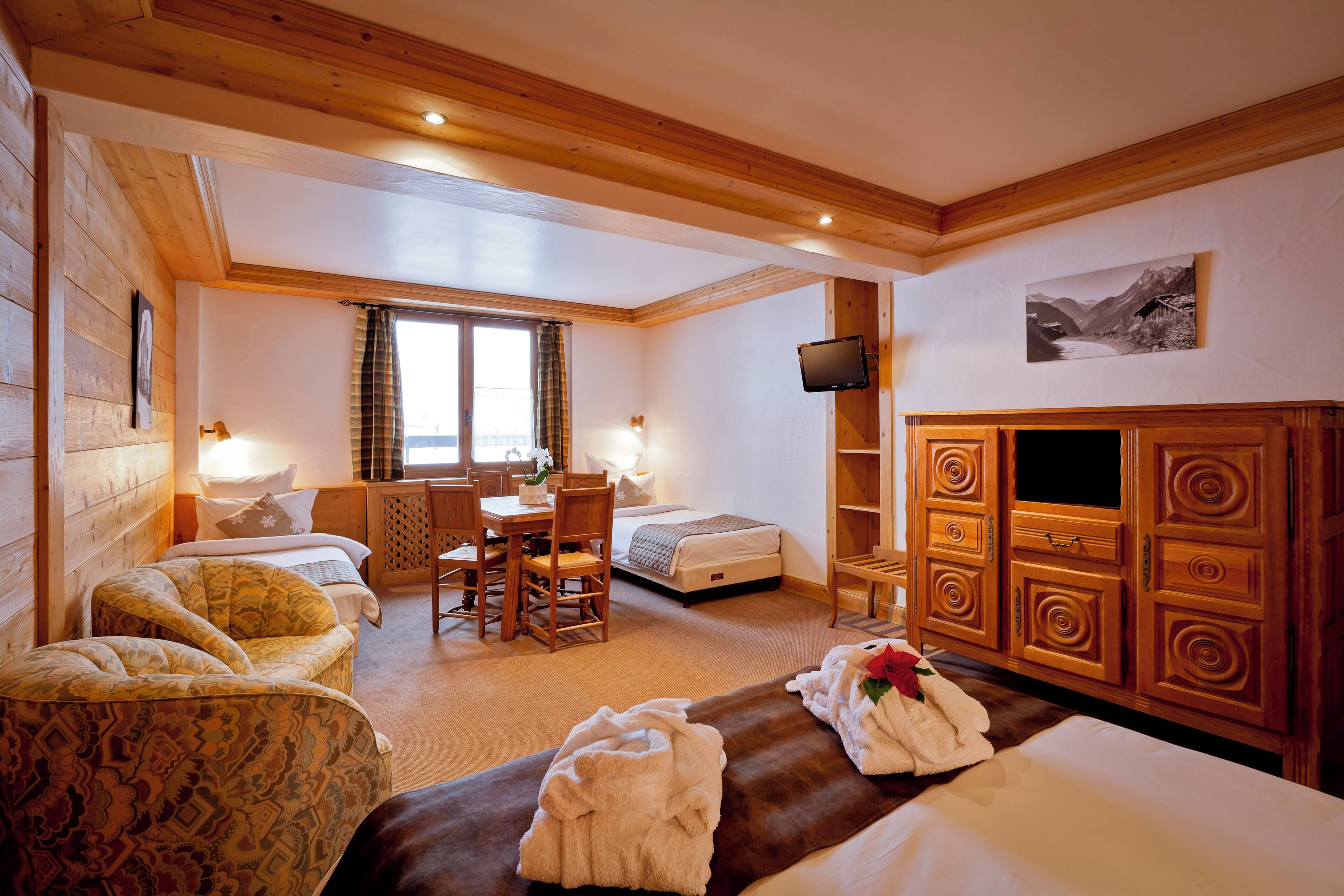 Une chambre d’hôtel confortable, avec un lit, deux fauteuils, un bureau, une télévision et une armoire en bois.