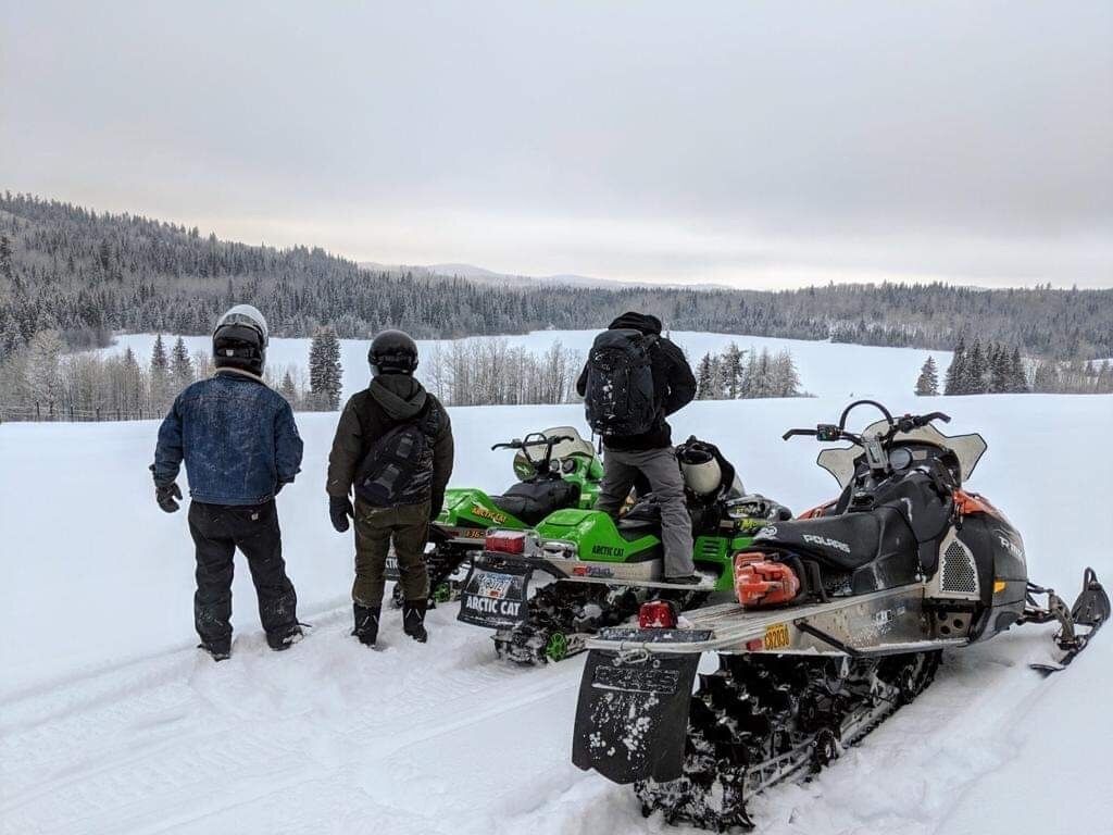 Drei Personen fahren auf Schneemotoren durch eine verschneite Landschaft.