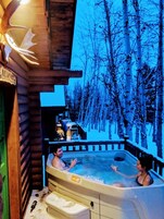 Una cabaña de madera con jacuzzi y vistas a un bosque nevado.