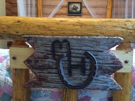 A rustic wooden sign with a horseshoe symbol, mounted on a wooden structure with a log beam above.