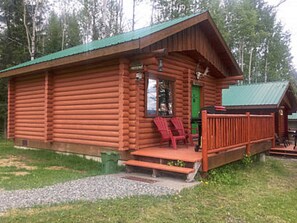 En timmerstuga med en veranda och två röda stolar.