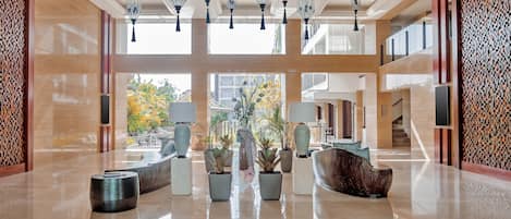 A spacious lobby with a polished floor, multiple seating areas, potted plants, and hanging light fixtures.