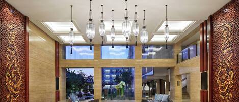 A spacious lobby with a high ceiling, multiple hanging light fixtures, and a central seating area with sofas and a coffee table.