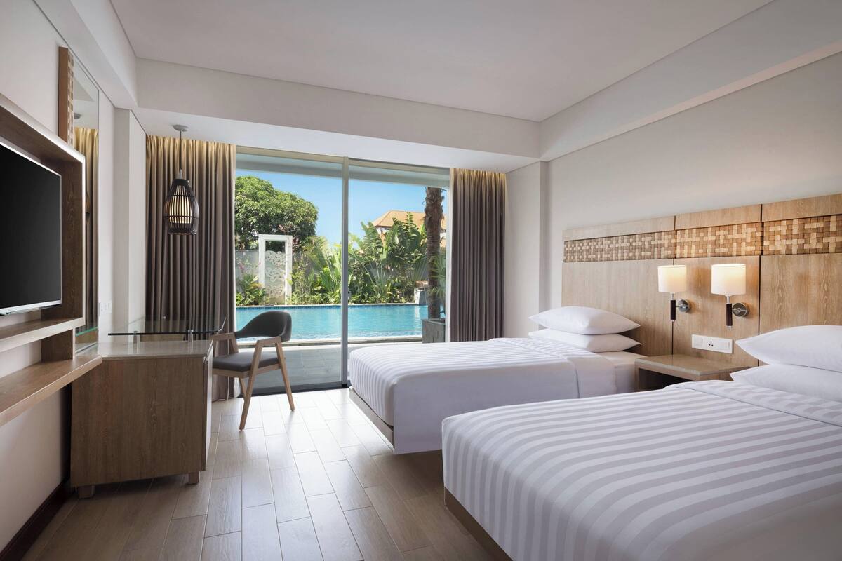 Ein Hotelzimmer mit zwei Betten, einem Schreibtisch, einem Fernseher und Blick auf einen Swimmingpool.