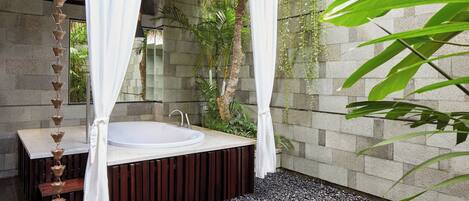 Un baño tipo spa con una bañera independiente, paredes de piedra y piso de grava.