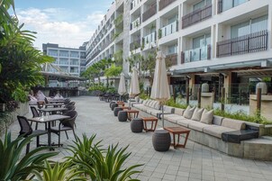 Un patio de hotel con mobiliario exterior, piscina y fachada de edificio moderna.