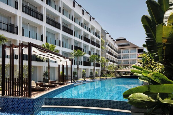 A hotel with a swimming pool surrounded by palm trees and lounge chairs. - Fairfield By Marriott Bali Legian (Legian)