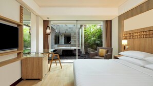 Habitación de hotel con cama, escritorio con silla, televisión, baño con lavamanos y espejo, y vista a zonas verdes.