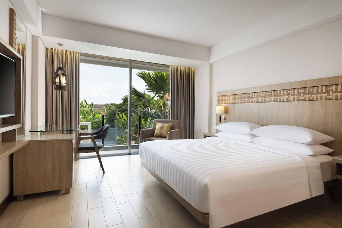 Ein modernes Hotelzimmer mit einem großen Bett, einem Schreibtisch, einem Sessel und einem Fernseher.