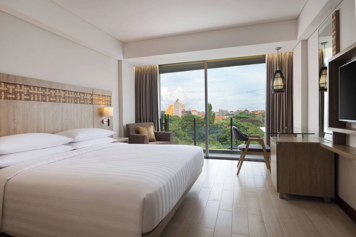 Ein modernes Hotelzimmer mit einem großen Bett, einem Schreibtisch und Blick auf die Stadt.