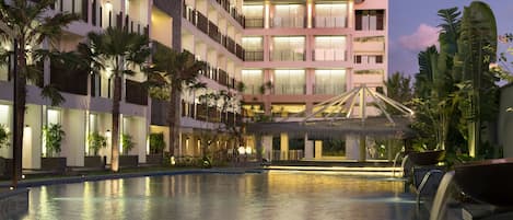 A hotel with a large swimming pool, multiple balconies, and a thatched-roof structure.