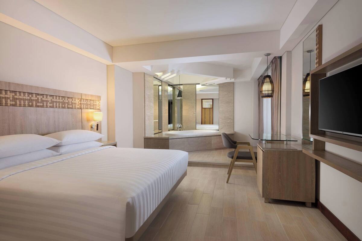 Ein modernes Hotelzimmer mit einem großen Bett, einem Schreibtisch, einem Flachbildfernseher und einer Glastrennwand.