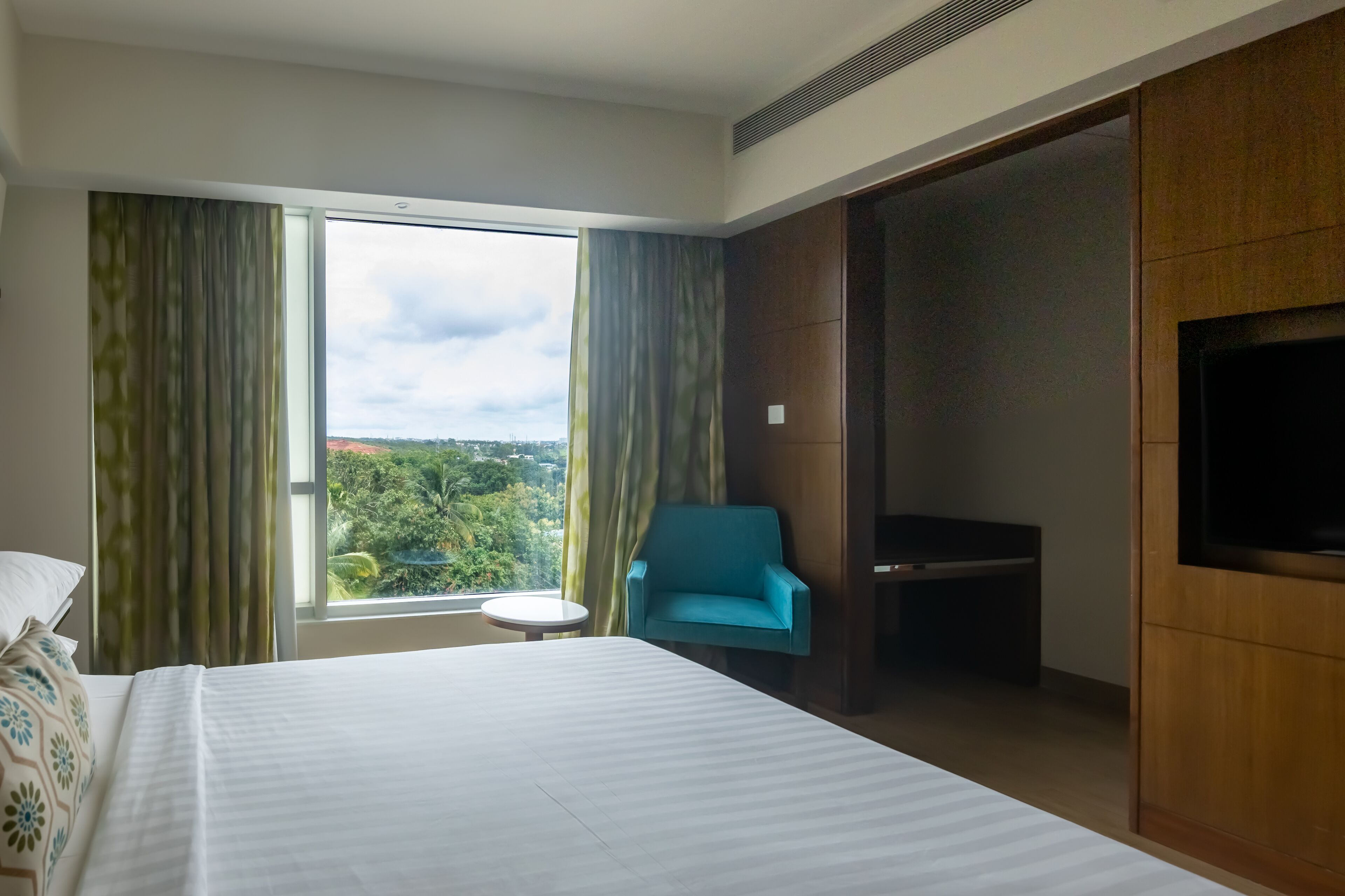 Habitación de hotel con una cama grande, televisión, una mesita y vistas al exterior.
