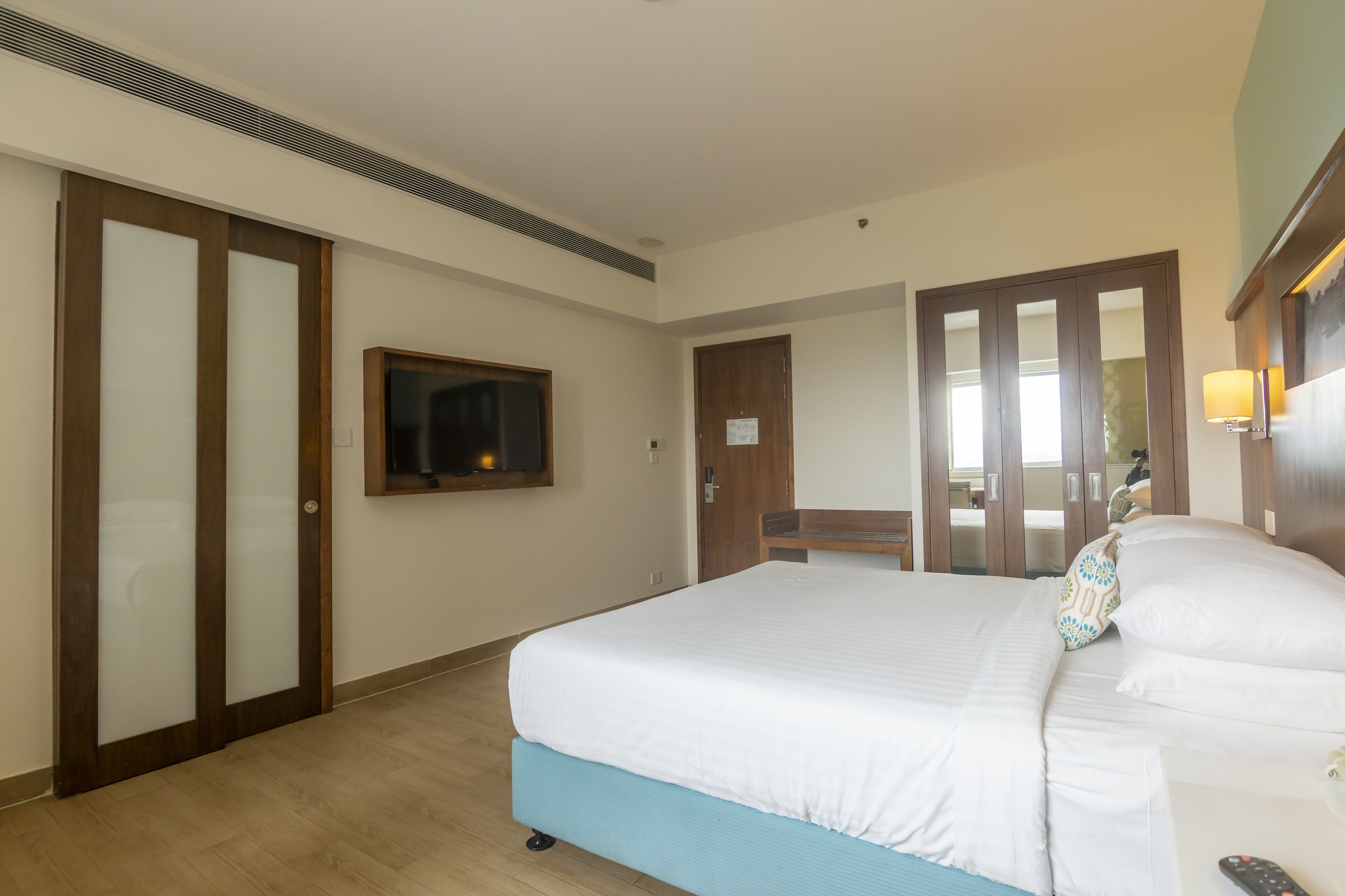 Une chambre d’hôtel avec un grand lit, un téléviseur fixé au mur, une armoire en bois et un miroir.