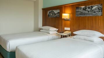 Une chambre d’hôtel avec deux lits simples, une tête de lit en bois, une table de chevet avec une lampe et deux tableaux accrochés au mur.