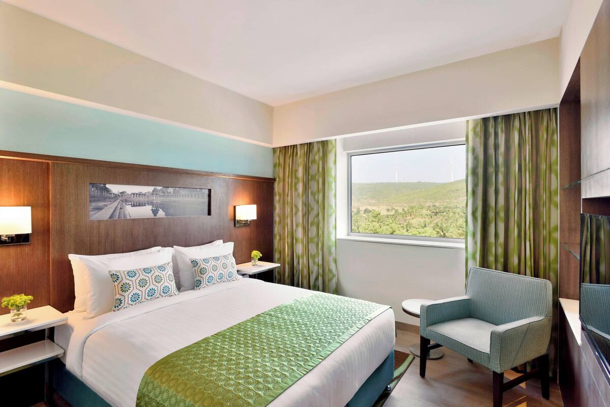 A hotel room with a large bed, a chair, a small table, and a TV.
