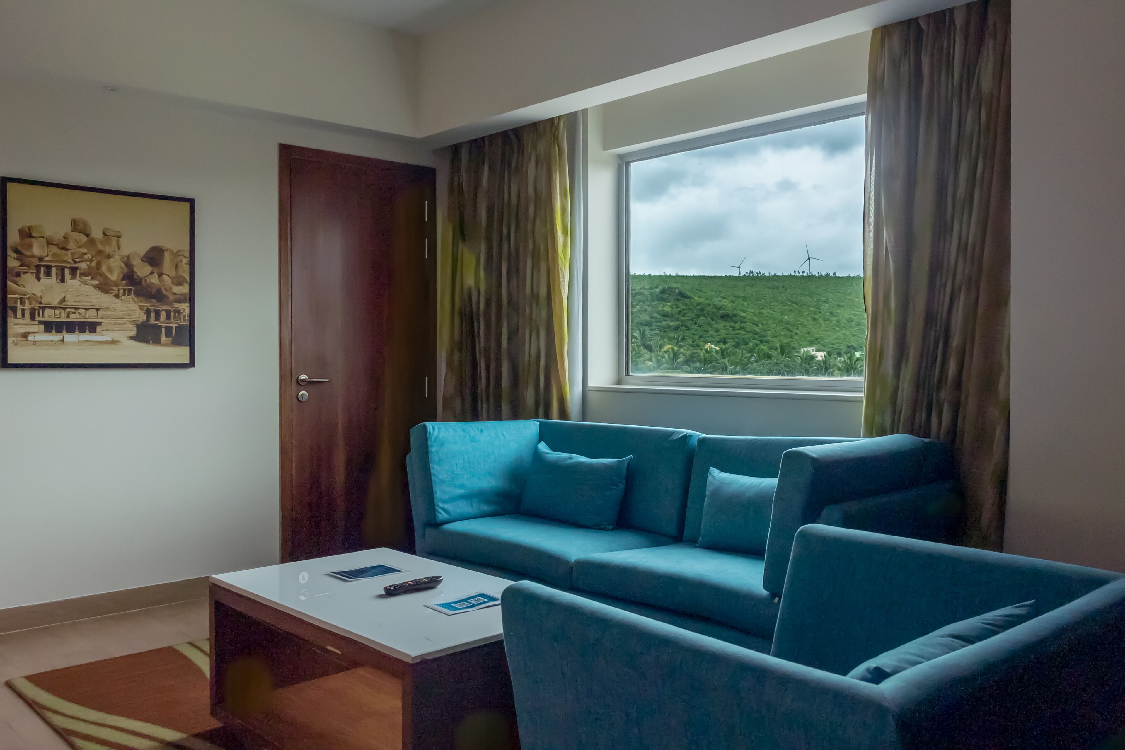 A room with a blue sofa, a white coffee table, and a view of wind turbines through a window.
