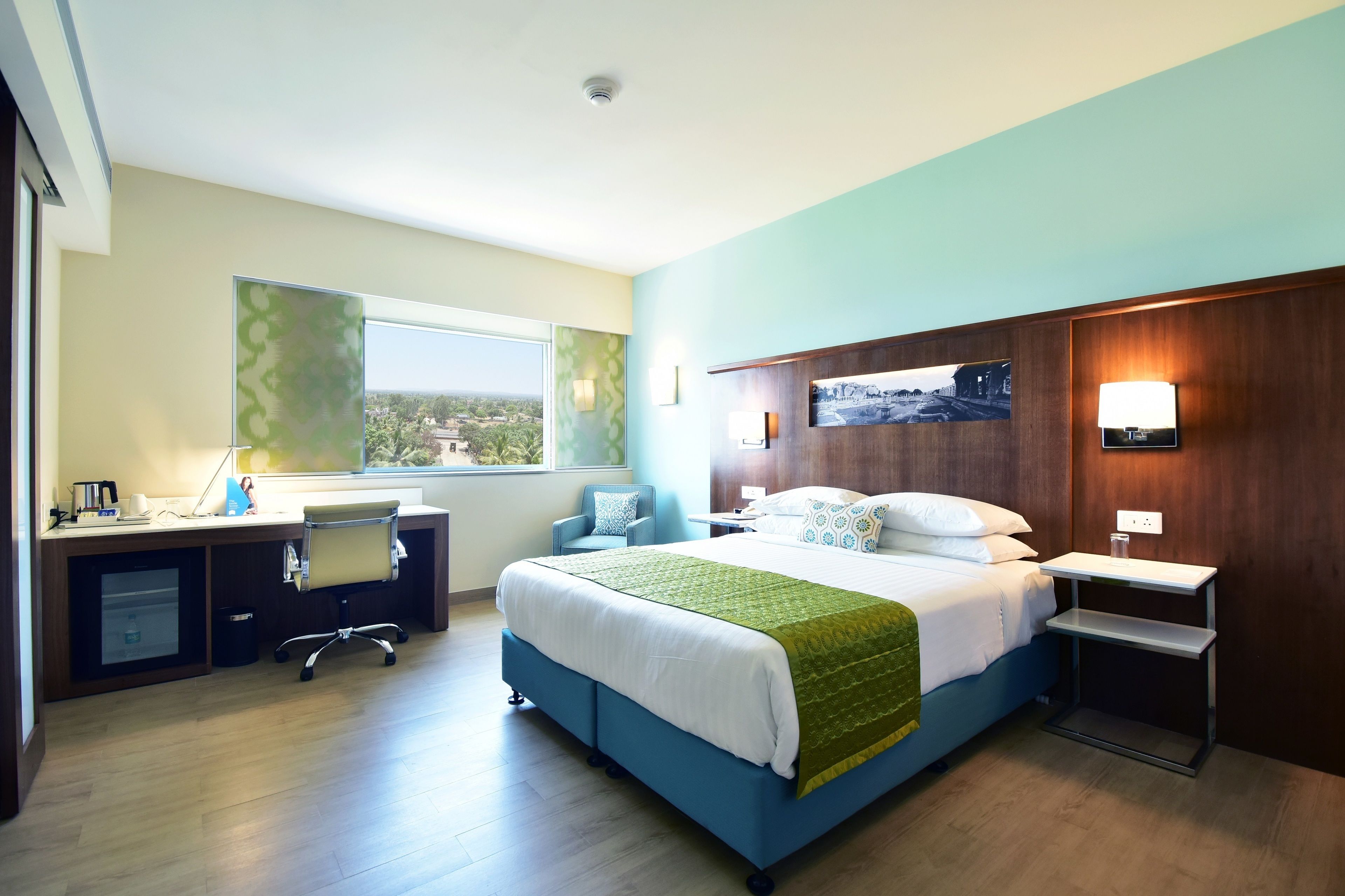 A hotel room with a bed, desk, chair, and a view of the outdoors.