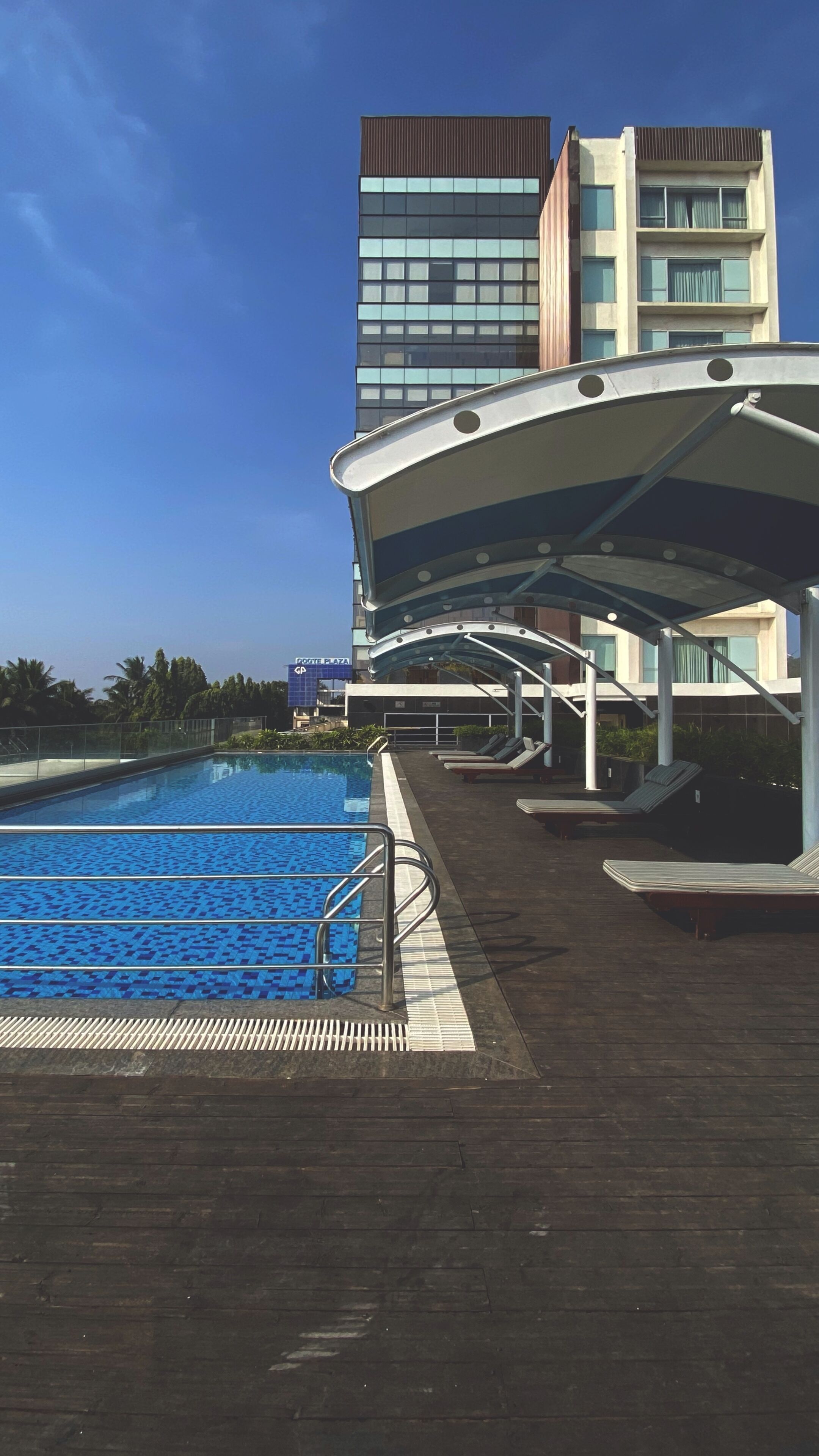A swimming pool with a wooden deck, lounge chairs, and a covered area.