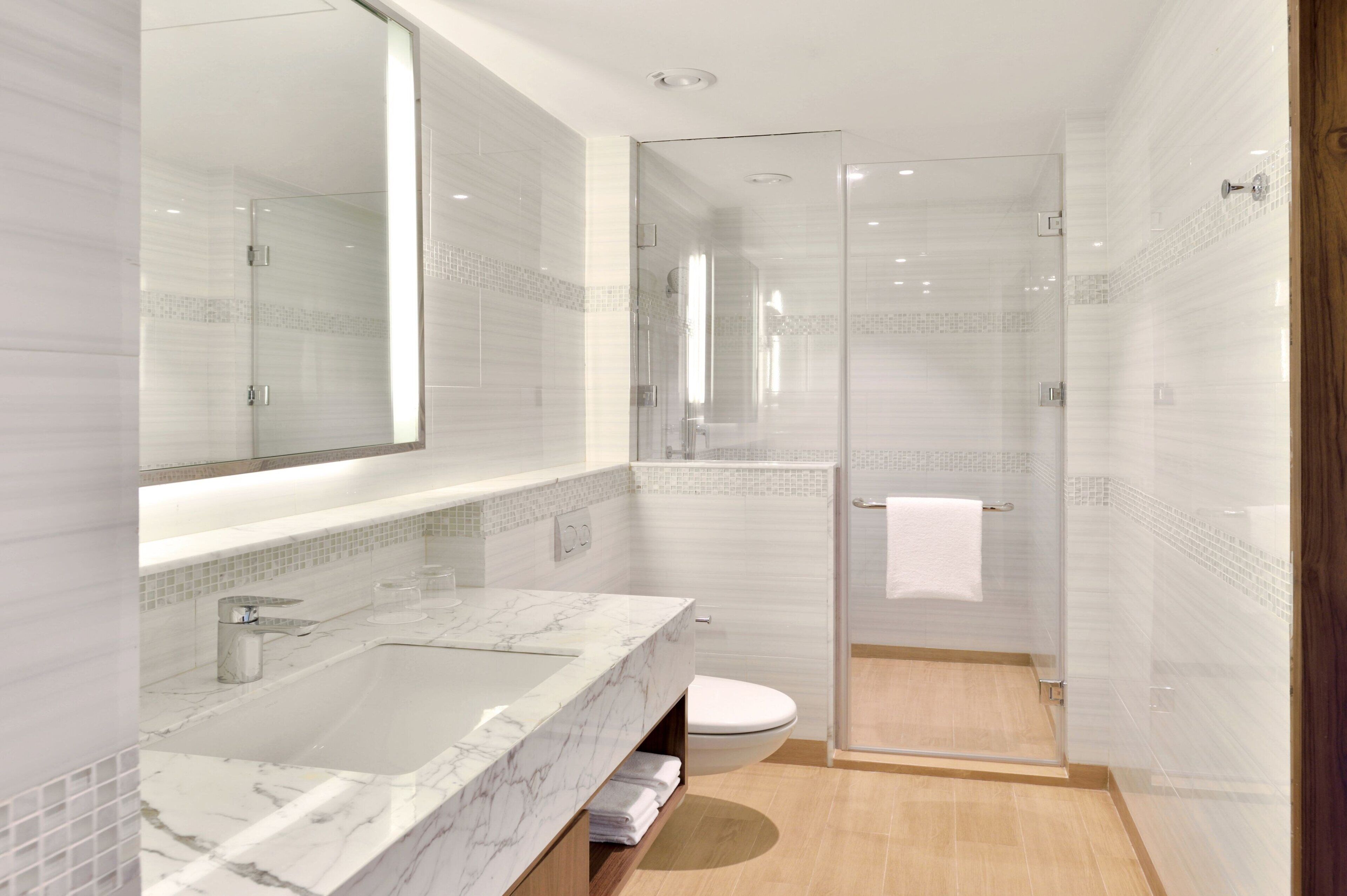 Et moderne badeværelse med en stor marmorvask, et brusekabine i glas og et toilet.