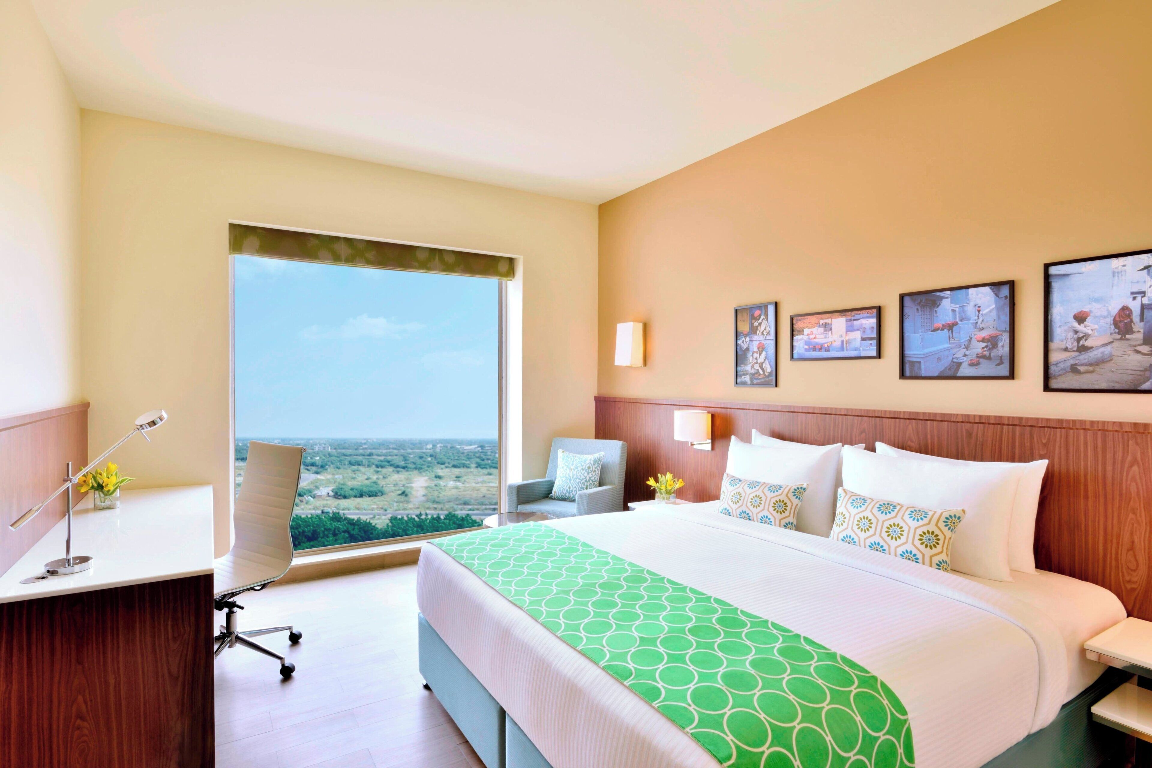 Une chambre d’hôtel avec un grand lit, un bureau, une chaise et une vue sur la ville.