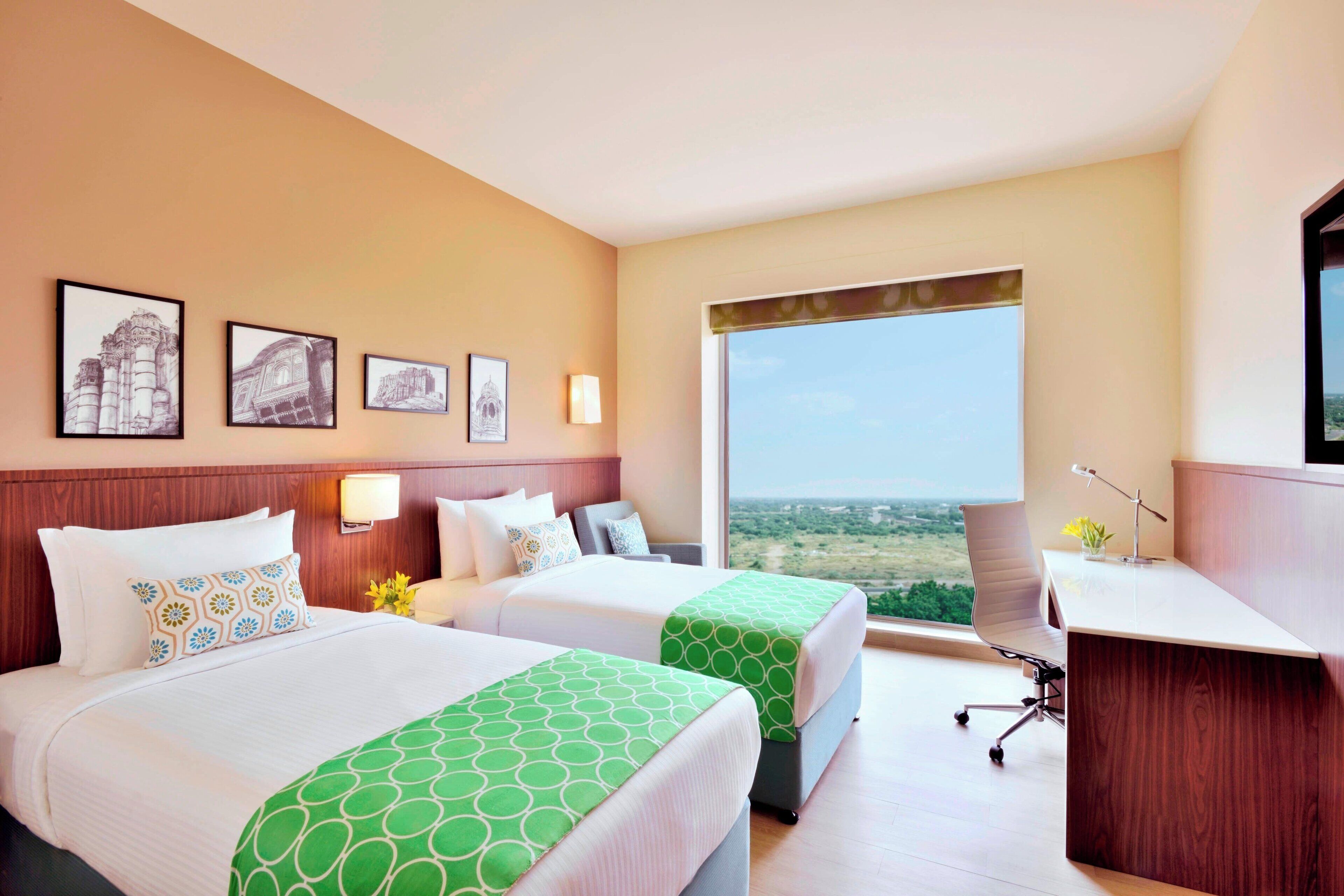 A hotel room with two beds, a desk, a chair, and a large window offering a view.