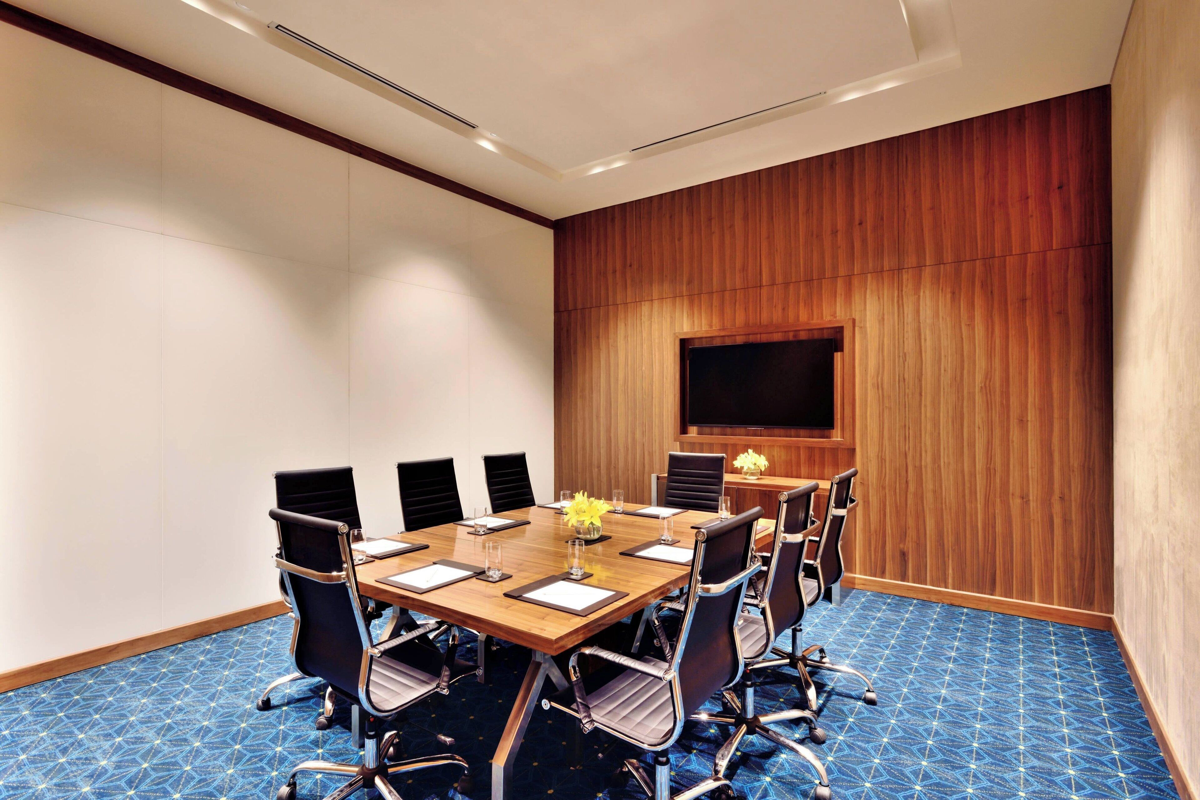 Un salón de conferencias con pared de paneles de madera, una pantalla grande y una alfombra azul estampada.