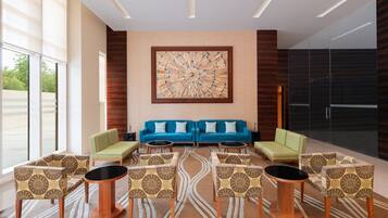 A modern lobby with a blue sofa set, patterned chairs, and a large abstract artwork on the wall.