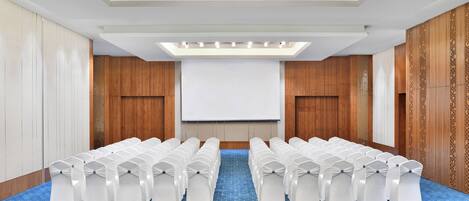 A conference room with rows of white chairs, a projector screen, and a patterned carpet.