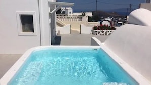 A swimming pool with clear blue water, surrounded by white walls and a white building in the background. - Ayoba Santorini (Santorini)