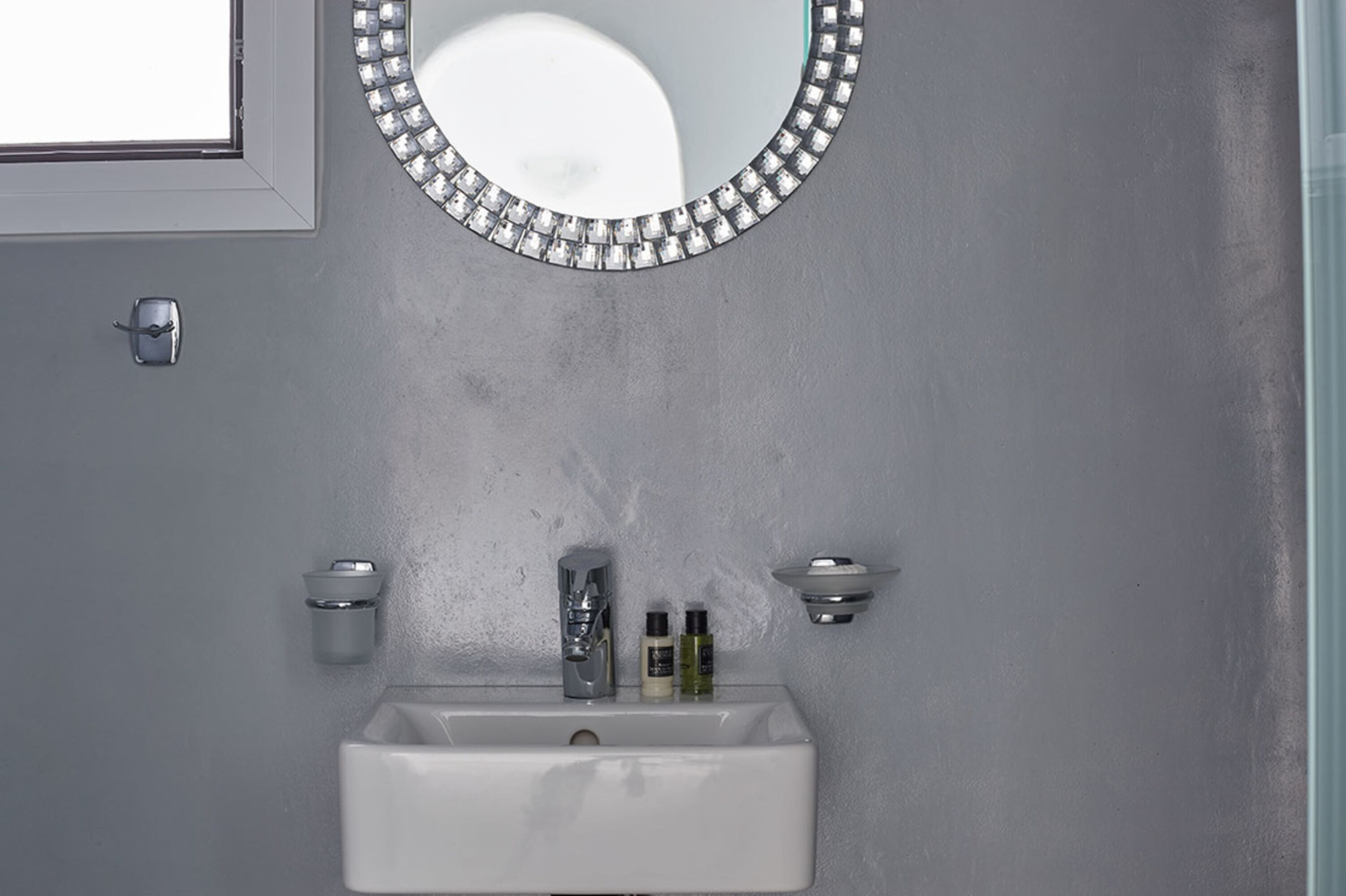 Un baño con un lavamanos blanco, un espejo con marco de forma de diamante y dos luces fijadas a la pared.