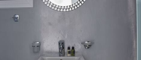 Un baño con un lavamanos blanco, un espejo con marco de forma de diamante y dos luces fijadas a la pared.