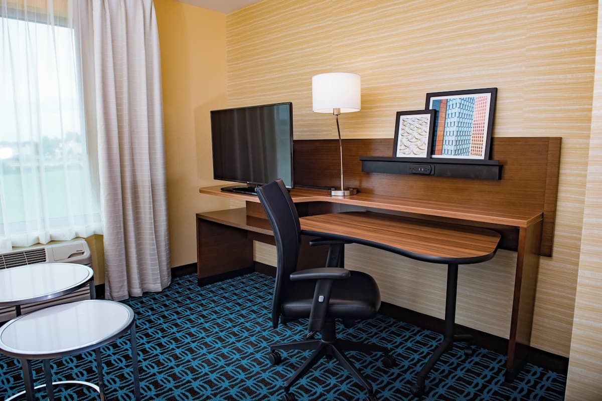 A hotel room with a desk, chair, TV, lamp, and two framed pictures on the wall.