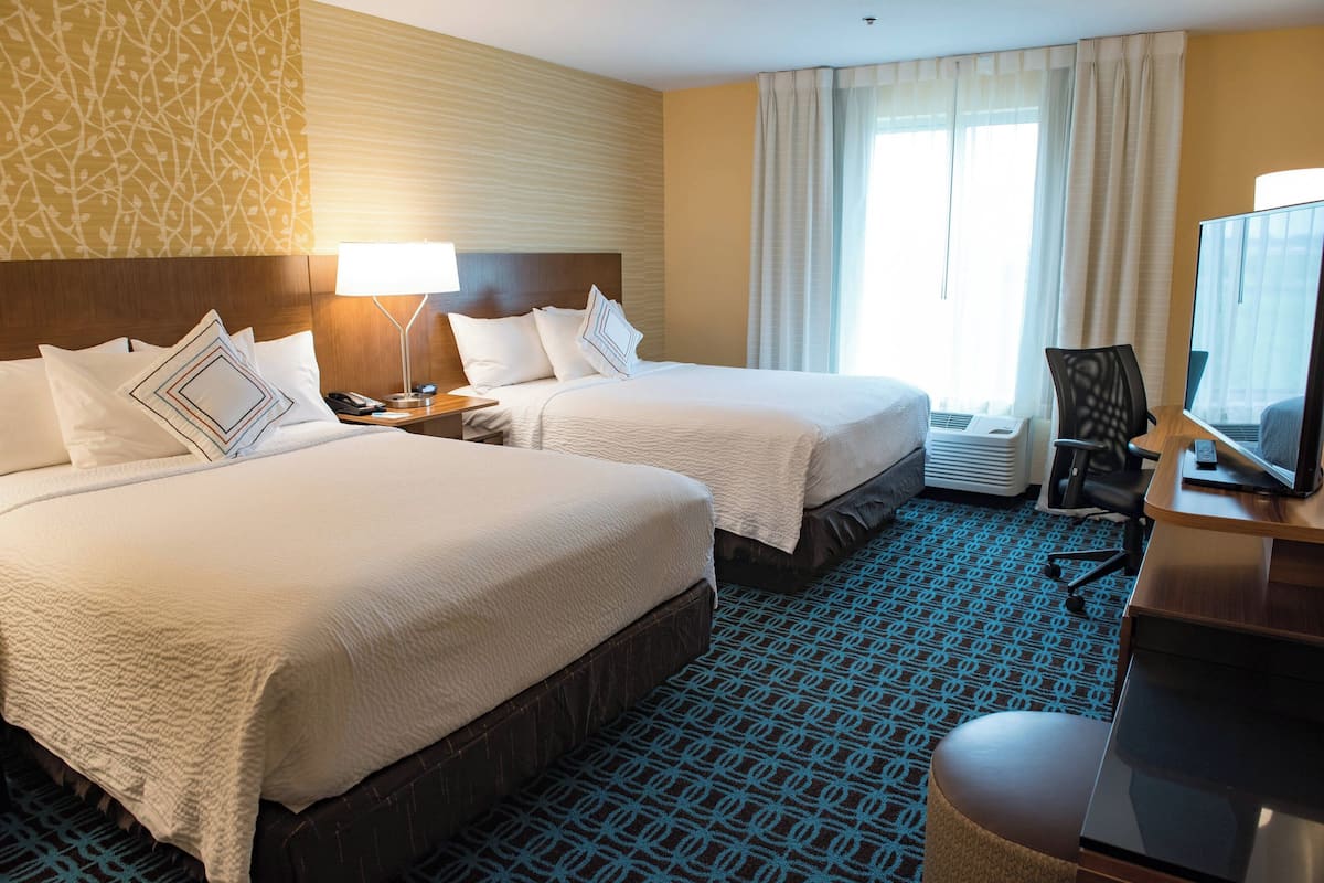 A hotel room with two beds, a desk with a computer, a chair, and a window with curtains.