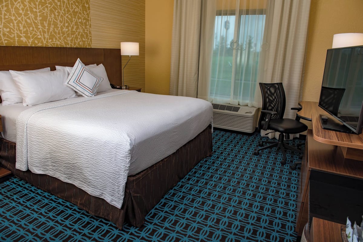 A hotel room with a large bed, a desk with a computer, and an air conditioning unit.