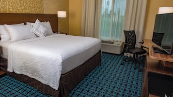 A hotel room with a large bed, a desk with a computer, and an air conditioning unit.