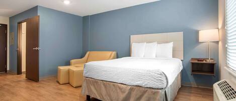 A hotel room with a bed, a chair, a nightstand, and a heater.