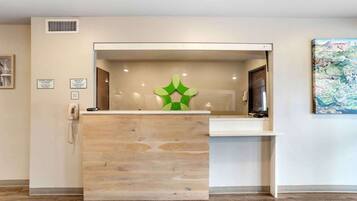 A reception desk with a wooden finish, a green decorative piece, and a check-in/out sign.