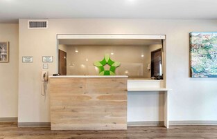 Una recepción con detalles de madera, un adorno verde y un cartel de registro de entrada y salida.