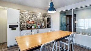 A modern kitchen with a wooden dining table, white chairs, a blue pendant light, and a tiled backsplash.