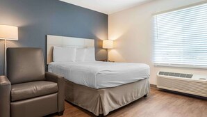A hotel room with a bed, a chair, two wall lamps, and a window with blinds.