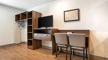 A compact room with a wooden desk, two chairs, a flat-screen TV, and a coat rack.
